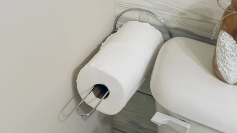 Paper towel holder mounted to a wall holding toilet paper