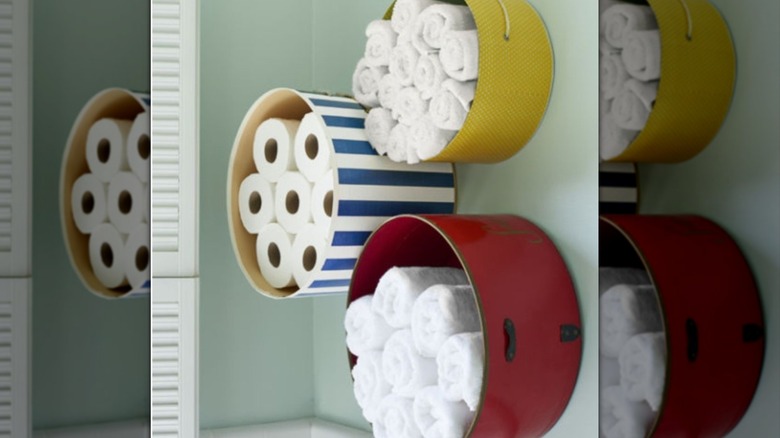 Three hat boxes mounted to the wall filled with toilet paper and towels