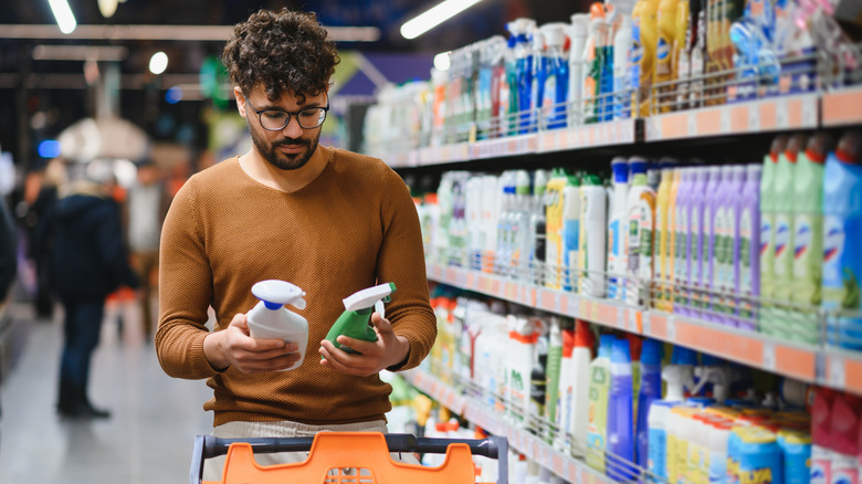 Person comparing two bottles of spray cleaner in a store.