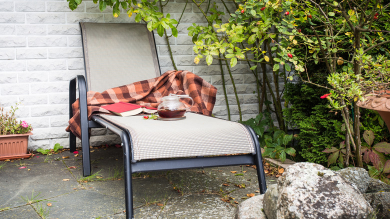 A lounge chair with a throw blanket on it as well as a pot of tea.