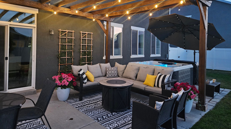 A concrete slab patio with a jacuzzi, patio furniture, and a rug on the ground.