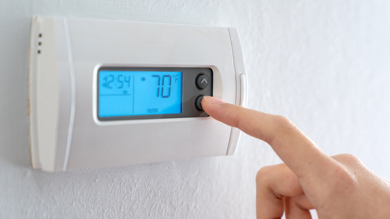 A woman is pressing the down button of a wall attached house thermostat