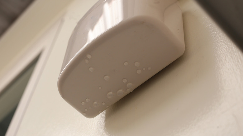 Wall-mounted drain pump for air conditioner with water droplets underneath, indicating malfunction or leakage