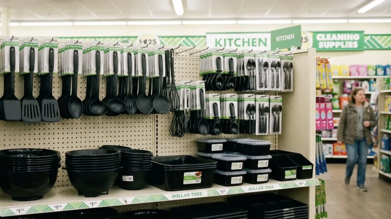 A woman walks through the kitchen section of Dollar Tree near an assortment of black plastic utensils
