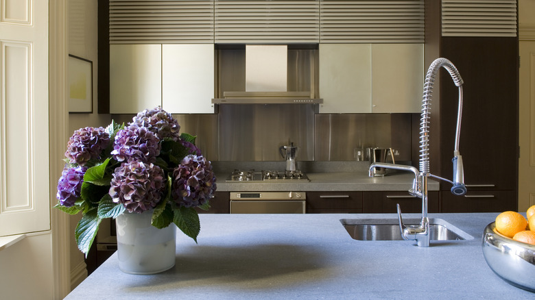 Purple hydrangeas sitting on a kitchen counter in front of a wall of stainless steel cabinets