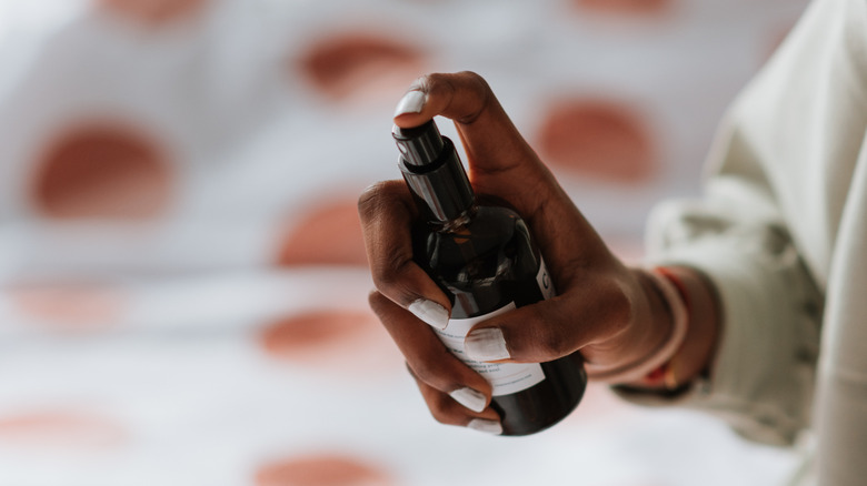 Woman spraying linen spray from amber glass bottle