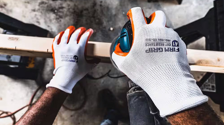 A person wears a pair of Firm Grip Nitrile Gloves while sanding a piece of lumber
