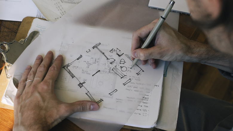 man sketching out a room layout on tracing paper