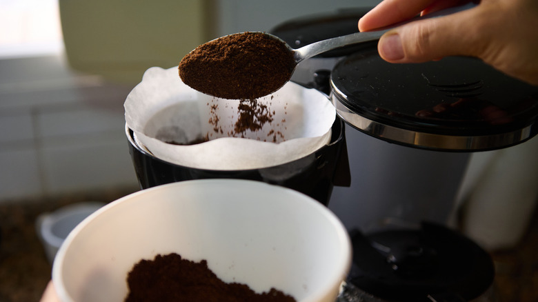 close up of hand spooning coffee grounds into filter