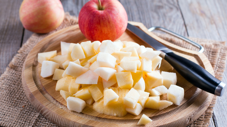 Whole and diced apples on a cutting board with a knife