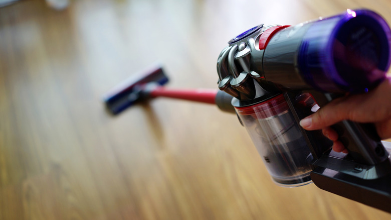 A person uses a Dyson cordless stick vacuum to clean a floor