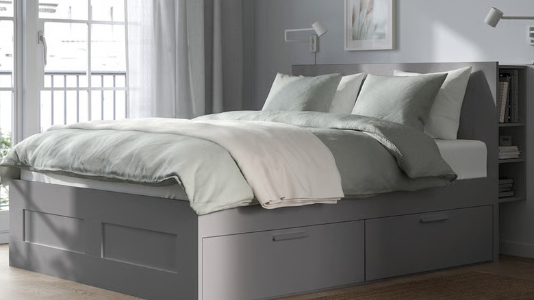 The BRIMNES Bed frame with storage & headboard in grey with a light green comforter in a grey room
