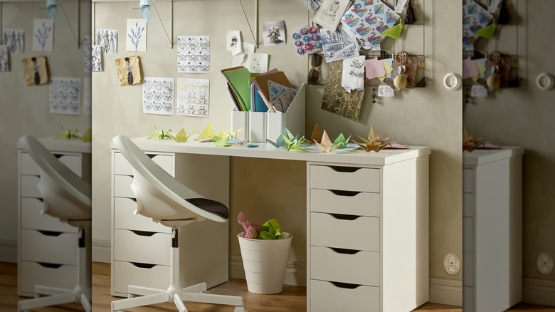 A white LAGKAPTEN / ALEX Desk in a girl's room with origami, folders, and papers on the wall