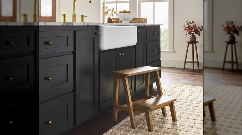 A small wooden step stool sits in front of a kitchen sink