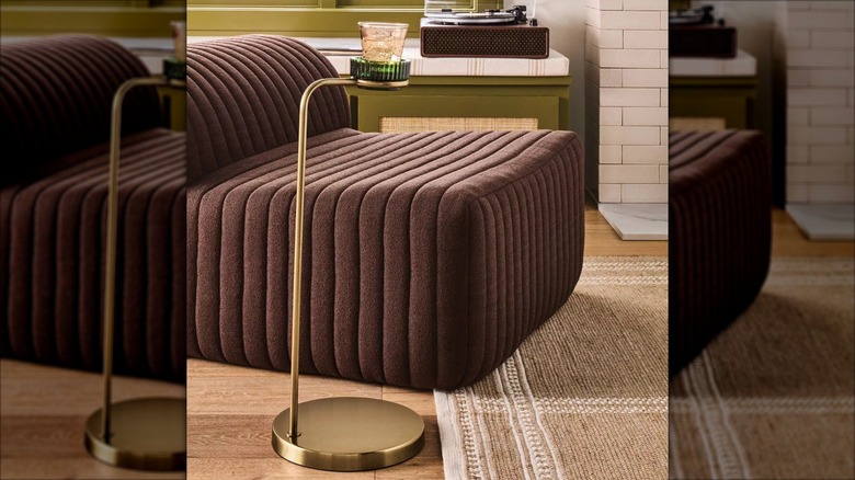 A small gold drinks table holds a glass near a modern brown chair