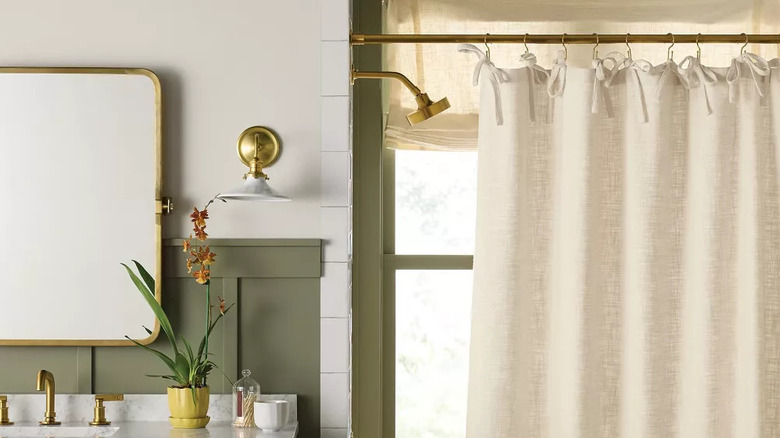 An oatmeal-colored shower curtain hangs in a green and white beathroom
