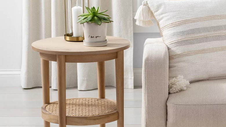 A candle and small potted plant sit on top of a wood and cane round accent side table