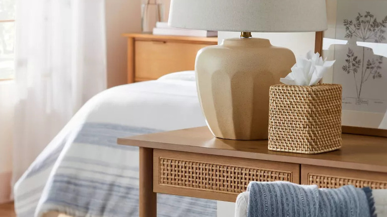 A woven tissue cover box sits next to a bedroom lamp on a console table