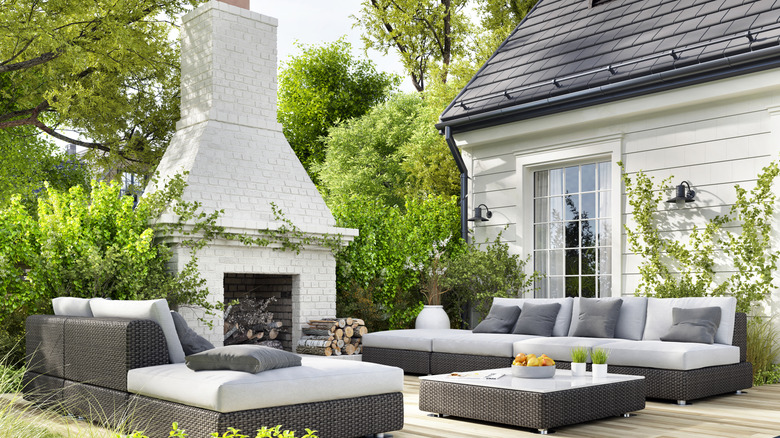A cozy outdoor living room with a large fireplace, throw pillows, and a blanket