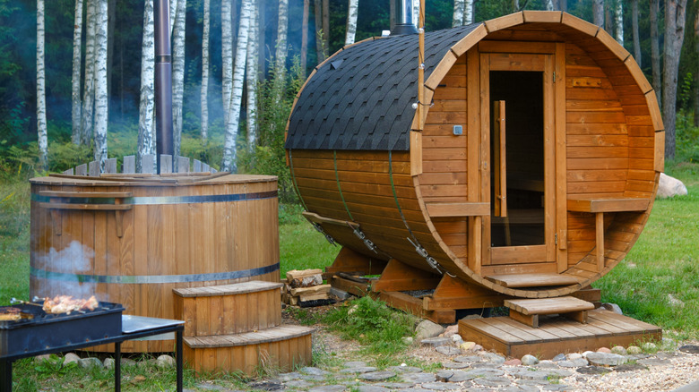 A backyard barrel sauna with a small wooden hot tub next to it