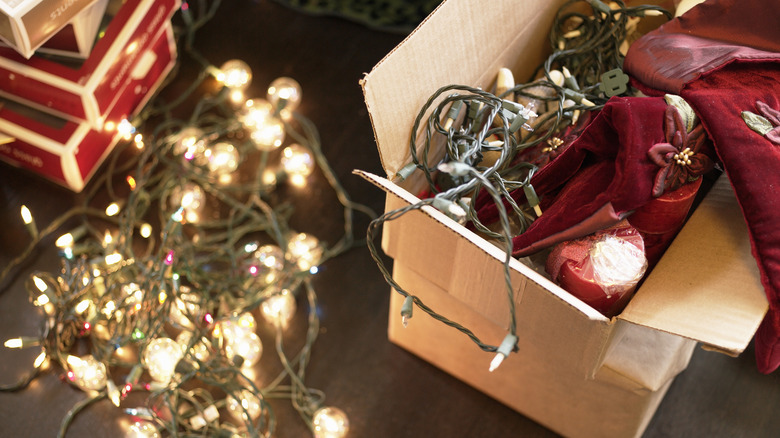 A box of Christmas decorations next to lit string lights on the floor