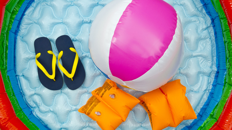 An inflatable pool with flip flops, a beach ball, and arm floaties