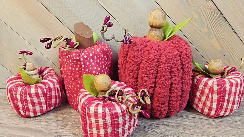 Several fabric-covered pool noodles shaped like fall apples sit on a wooden table