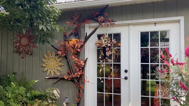 A large decorative branch hangs on a sage green home's exterior wall next to a french door
