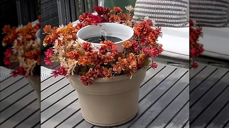 Faux autumn mums in a beige planter surround a small solar fountain