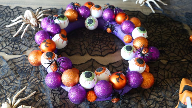 A glittering Halloween wreath sits on a table covered in a lacy spiderweb tablecloth