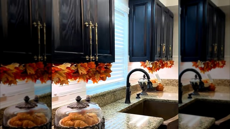 Two black kitchen cabinets are decorated underneath with faux autumn leaves