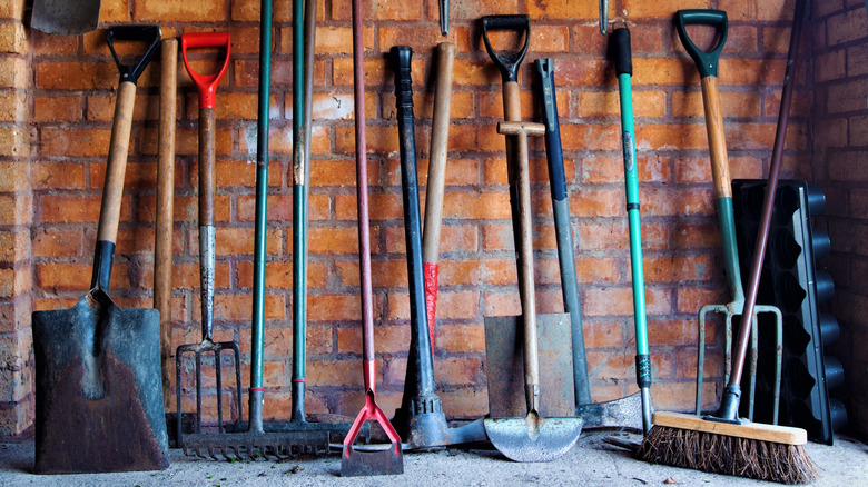 assortment of garden tools against a brick wall