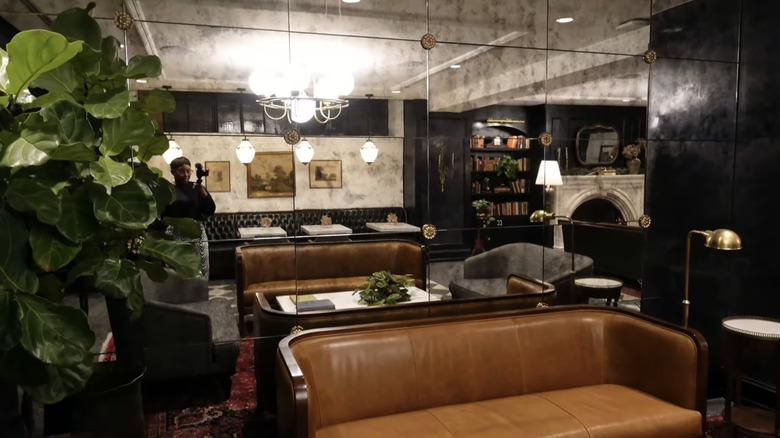 A leather sofa and fiddle leaf fig plant sit in front of an antique mirrored wall