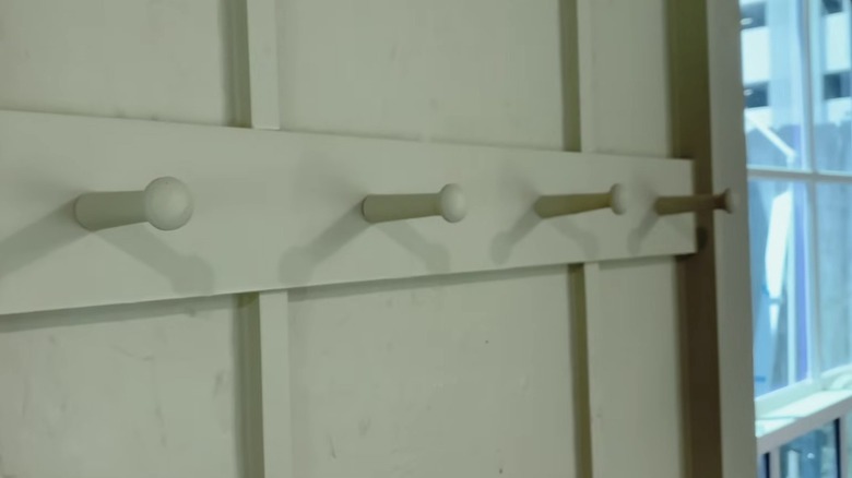 Four wooden coat pegs stick out from a green wall