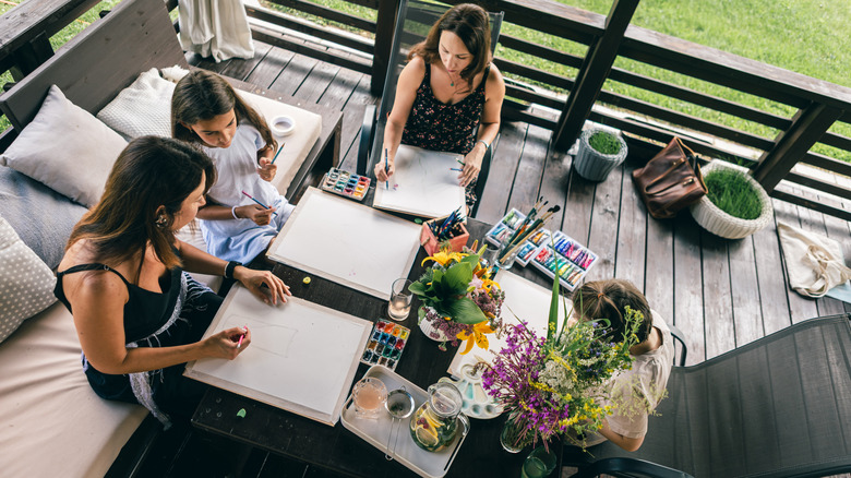 An overhead shot of people painting around a table on a wooden deck.