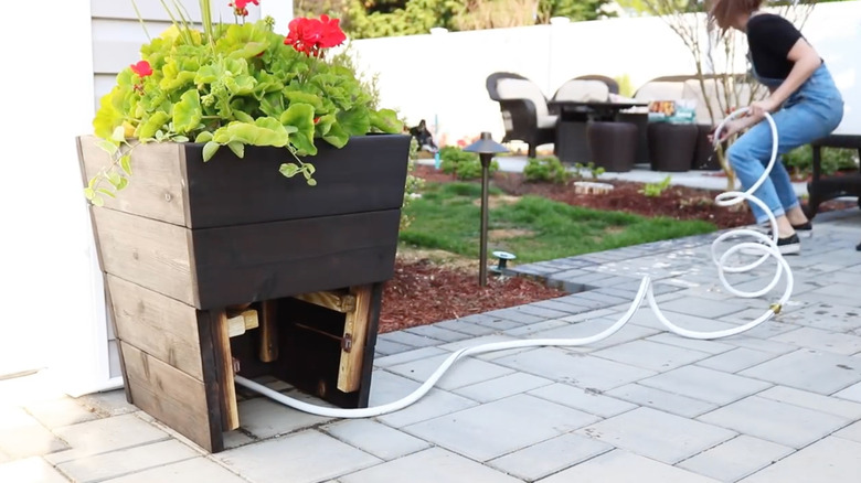 A person uses a white hose stored inside a hidden compartment of a deck planter.