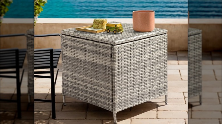 A terracotta pot and small toy van sit on a gray wicker deck side table.