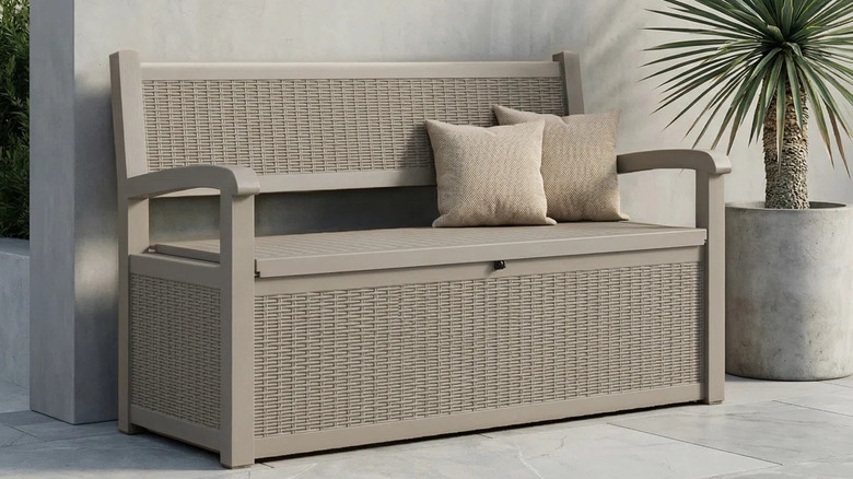 A beige storage bench on a deck next to a potted tropical plant.