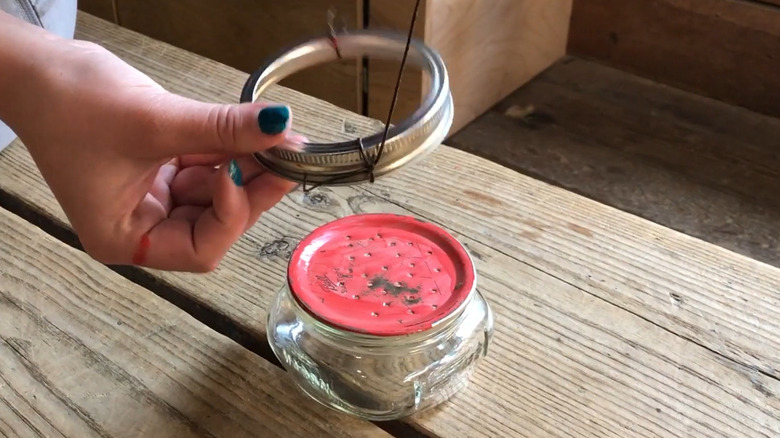 A Mason jar hummingbird feeder with a red lid with holes in it
