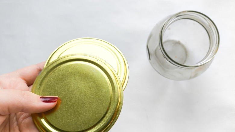 Hand holding two mason jar lids with empty mason jar in the background