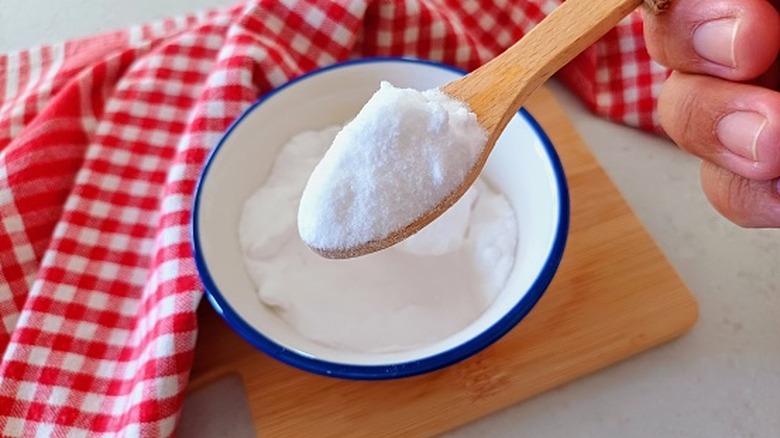 A person scooping a spoonful of baking soda out of a dish