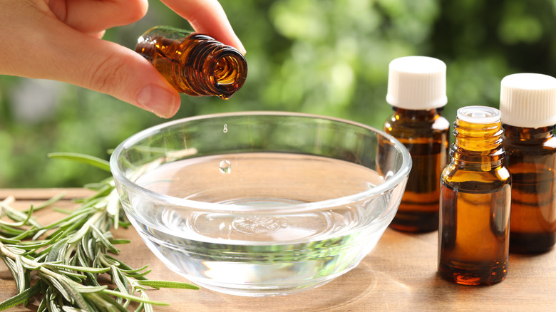 A person dripping essential oils into a glass bowl full of water