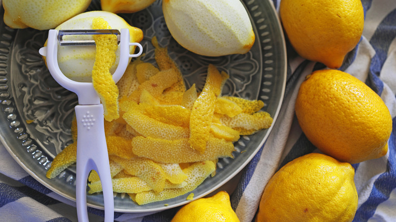 A bowl full of lemon peels, peeled lemons, and a peeler