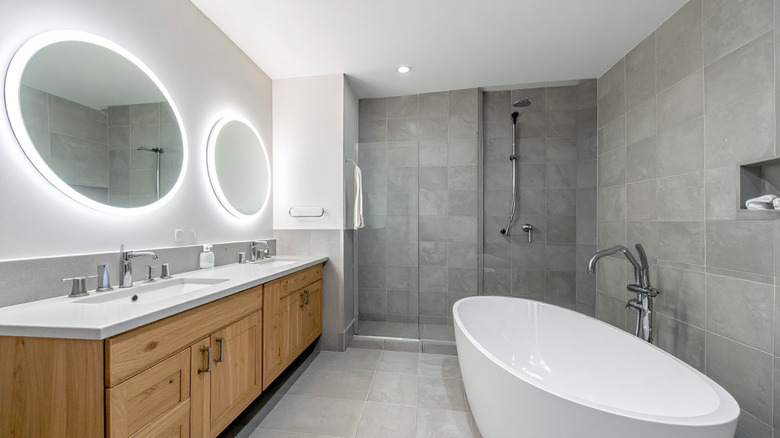 Gray tiles on walls and floor of contemporary bathroom with stand alone tub and wooden vanity
