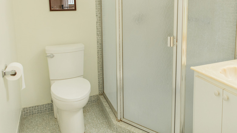 Bathroom with gray 1x1 tiles surrounding toilet and shower stall