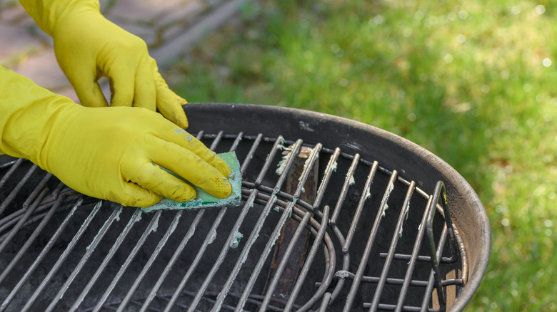 Gloved hands holding a sponge to clean dirty grill grates