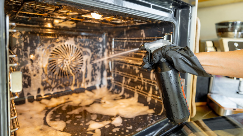 A gloved hand spraying oven cleaner into an open oven