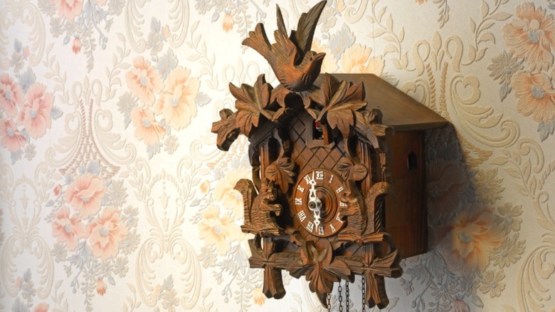 A wooden cuckoo clock on the wall with a peach, floral wallpaper