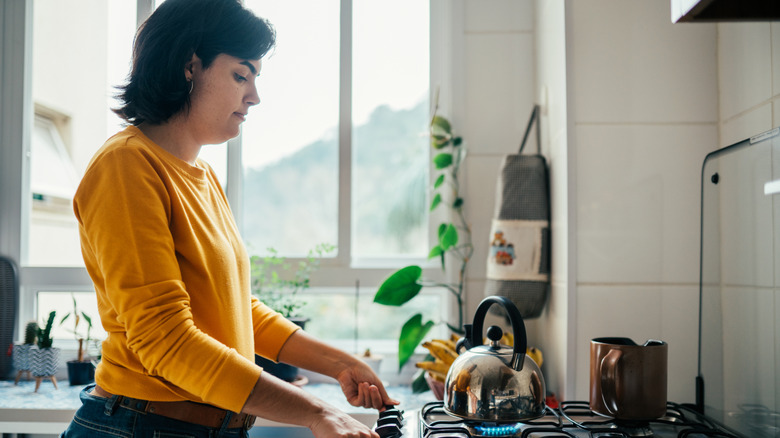Woman turning on gas stovetop to boil water in kettle