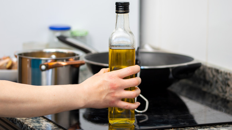 Hand holding a bottle of olive oil while cooking on stove